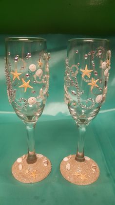 two wine glasses with starfish and seashells painted on them sitting side by side