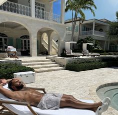 a man laying on top of a beach chair next to a swimming pool in front of a house