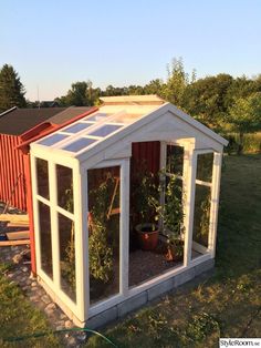 a small white greenhouse with plants growing in it's side wall and windows on the roof