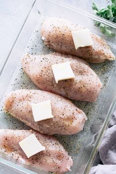 three pieces of raw chicken in a glass dish with parmesan cheese on top