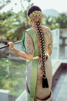 a woman wearing a green and white sari with braids on her head standing next to a railing