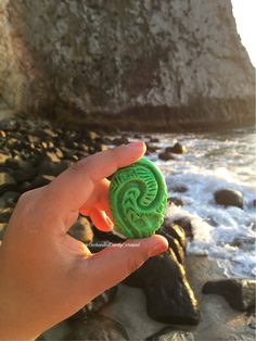 someone is holding up a green cookie in front of the ocean with rocks and water