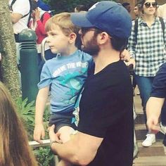 a man holding a small boy in his arms while standing next to other people on the street