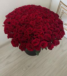 a large bouquet of red roses in a black vase on the floor next to a white wall