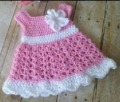 a pink and white crocheted dress laying on top of a wooden floor next to scissors