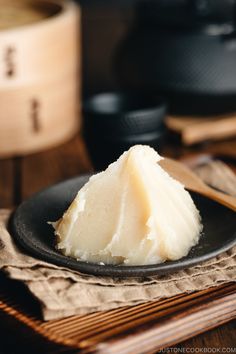 a piece of cheese on a black plate next to chopsticks and a wooden spoon