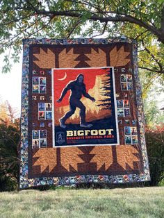 a bigfoot quilt hanging on the side of a tree in front of some trees