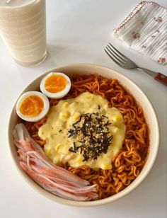 a bowl filled with noodles, eggs and meats next to a glass of milk