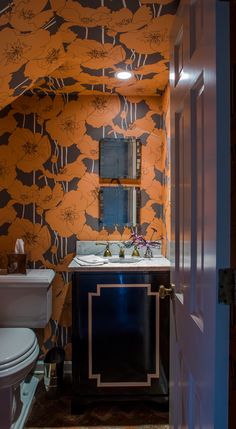 a bathroom with orange and black wallpaper on the walls, white toilet and sink