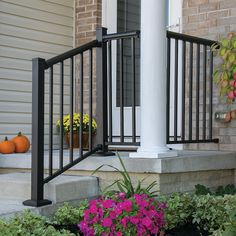 the front porch is decorated with flowers and pumpkins on the side walk, along with an iron railing