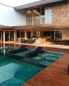 an indoor swimming pool in front of a large house with wooden decking and glass doors