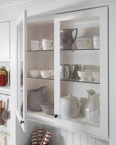 a kitchen with white cupboards filled with dishes and cups on top of shelves next to each other