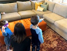 three children are standing in front of a couch pointing at something on the floor behind them