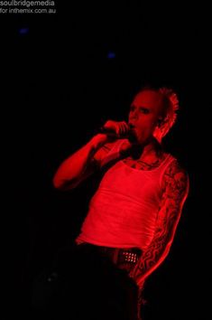 a man with tattoos on his arms and chest singing into a microphone in the dark