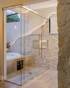 a bathroom with a stone wall and glass shower enclosure in the corner, next to a wooden floor