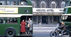 two double decker buses parked in front of a building with people standing on the sidewalk