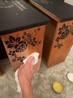 a person wiping down some wood with a cloth on the floor next to two wooden boxes