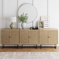 a sideboard with two vases and a round mirror on it next to a lamp