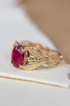 a gold ring with a red stone in it sitting on a white piece of paper