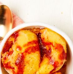 a bowl filled with bananas and sauce next to two spoons on top of a table