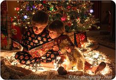 two young children sitting on the floor in front of a christmas tree reading a book