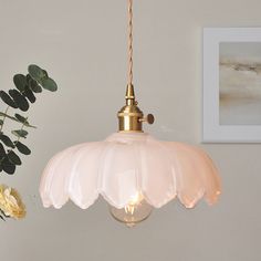 a light hanging from a ceiling next to a vase with flowers on the wall behind it