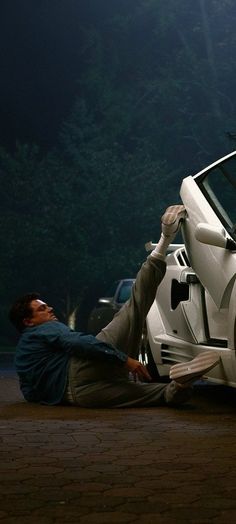 a man laying on the ground next to a car with its door open and another person leaning over it