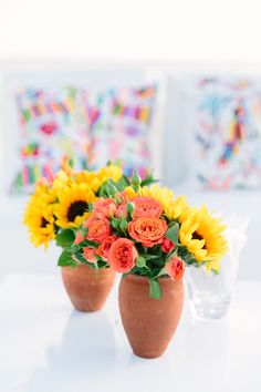 two vases with sunflowers and roses in them sitting on a white table