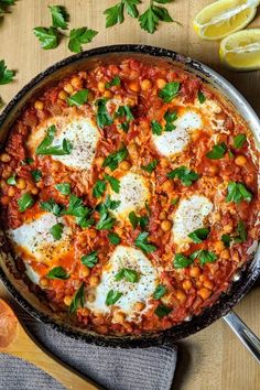 a skillet filled with baked beans and eggs on top of a wooden table next to sliced lemons