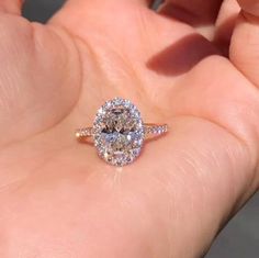 a close up of a person's hand holding a ring with an oval shaped diamond