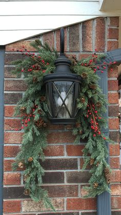 a lamp hanging from the side of a brick building decorated with evergreen and red berries