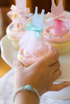 two cupcakes with pink frosting and blue bows on top are being held by a woman's hand