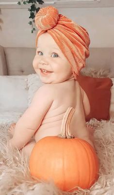 a baby sitting on top of a bed next to a large orange pumpkin and wearing a turban