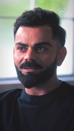 a close up of a person with a beard wearing a black shirt and looking at the camera