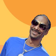 a man with sunglasses and a necklace on his neck smiles at the camera while standing in front of an orange background