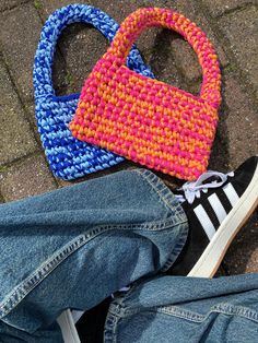 two purses sitting next to each other on the ground near someone's feet