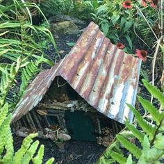 a bird house made out of corrugated sheet in the garden with ferns and flowers around it