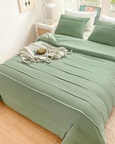 a bed with green sheets and pillows on top of it in a room next to a window