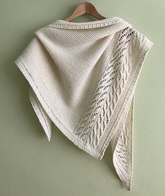 a white knitted shawl hanging on a green wall next to a wooden hanger