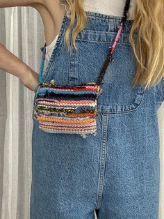 a woman wearing overalls with a multicolored purse on her back