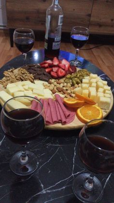 two glasses of wine are sitting on a table with cheese, fruit and crackers