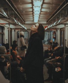 a woman standing on a subway train looking up at the sky with her eyes closed