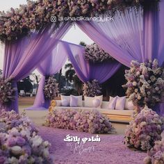 an outdoor wedding setup with purple drapes and flowers on the ceiling, couches and tables