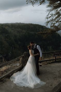 a bride and groom kissing on top of a mountain