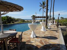 an outdoor dining area with tables and umbrellas next to a swimming pool in the background