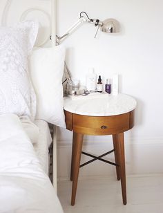 a table with some bottles on it next to a white bed and pillows in a room