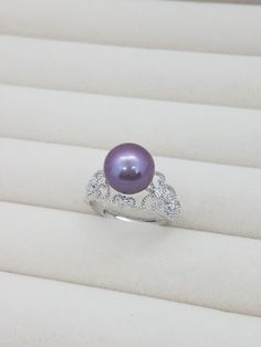 a purple pearl and diamond ring sitting on top of a white cloth covered box,