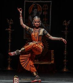 a woman in an orange and yellow outfit is doing a dance move with her arms outstretched