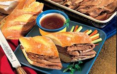 a sandwich cut in half on a blue plate with dipping sauce and bread sticks next to it