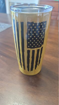 a yellow cup with an american flag painted on the side sitting on a wooden table